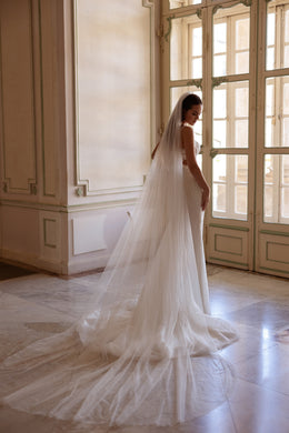 Rear view of an ivory mermaid wedding dress with a long sheer train and a veil draped over the fitted gown