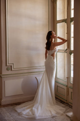 Profile of an ivory mermaid wedding dress with a fitted lace bodice, narrow straps, and a sweeping train