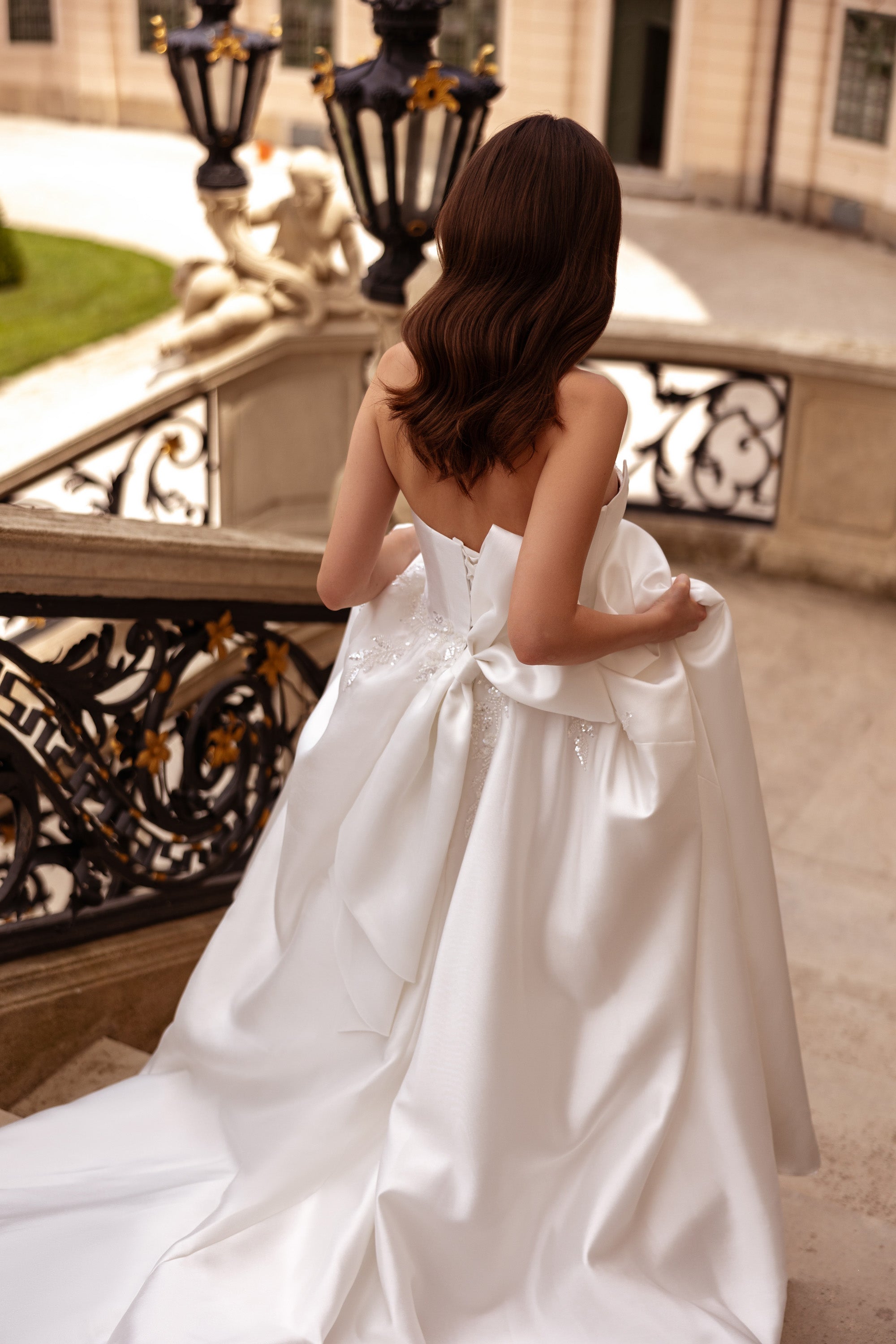 Back view of an ivory wedding dress with a strapless bodice, waist bow, and long flowing train