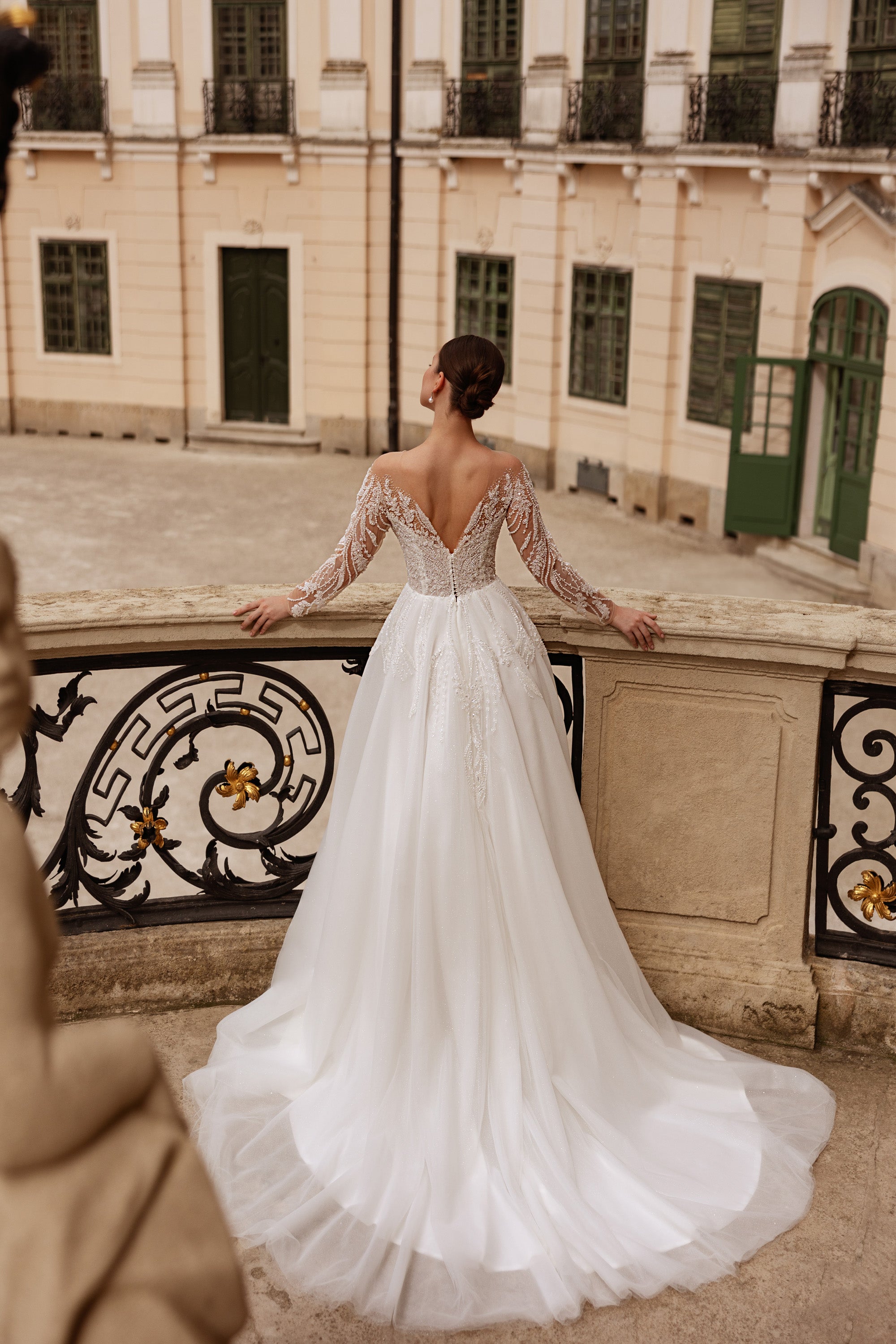 Back view of an ivory wedding dress with a V-shaped lace back, long sleeves, and a flowing train