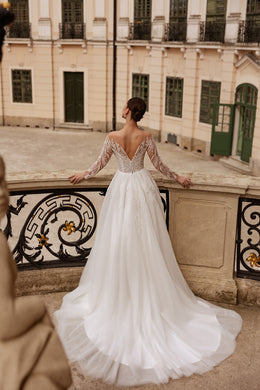 Back view of an ivory wedding dress with a V-shaped lace back, long sleeves, and a flowing train