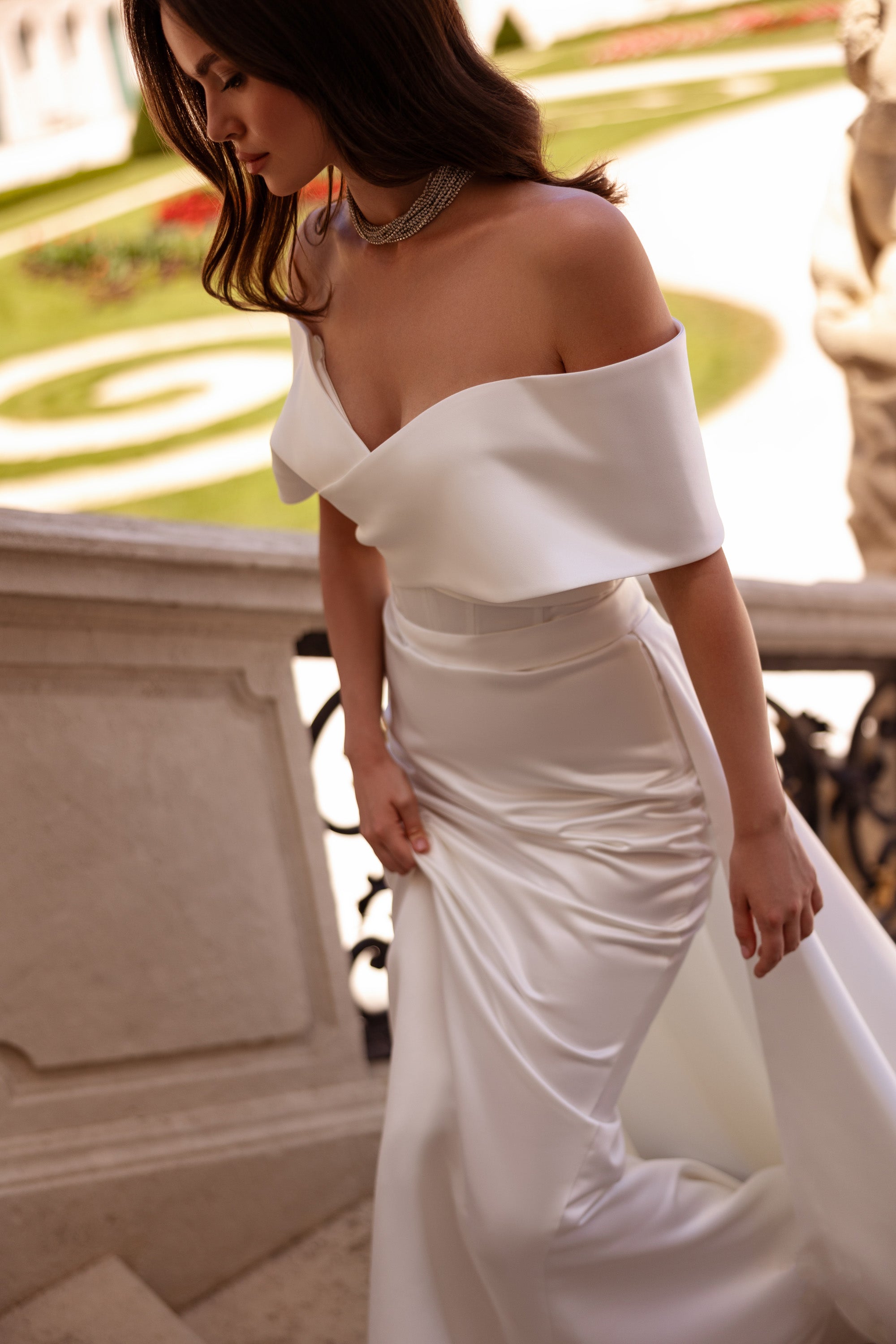 Ivory wedding dress with an off-the-shoulder draped neckline, fitted ruched skirt, and flowing train