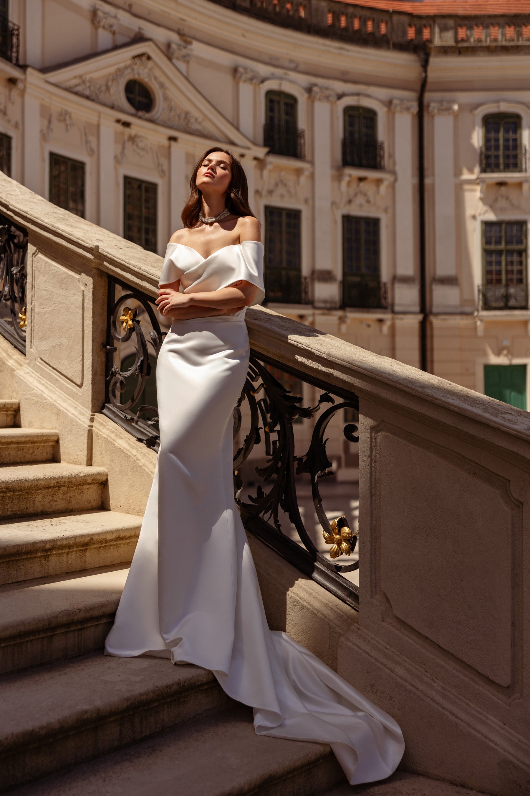Sleek ivory sheath wedding dress with an off-the-shoulder neckline and long draped train