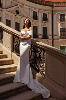 Sleek ivory sheath wedding dress with an off-the-shoulder neckline and long draped train