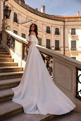 Ivory wedding dress shown from behind with an off-the-shoulder neckline and wide flowing train