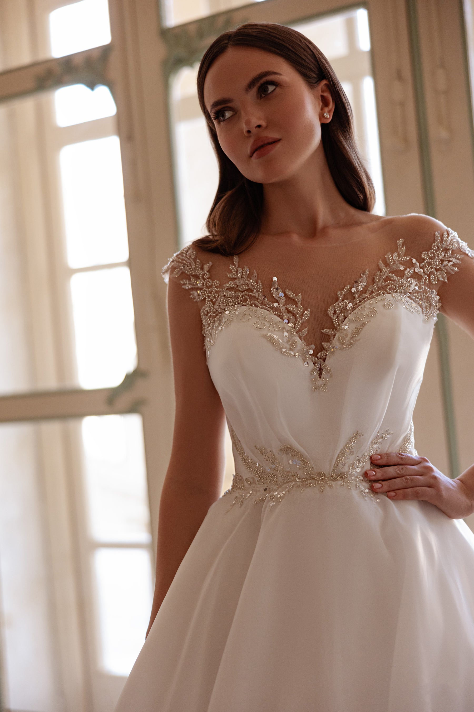 Close-up of an ivory wedding dress with a sheer beaded neckline and sparkling waist embellishment