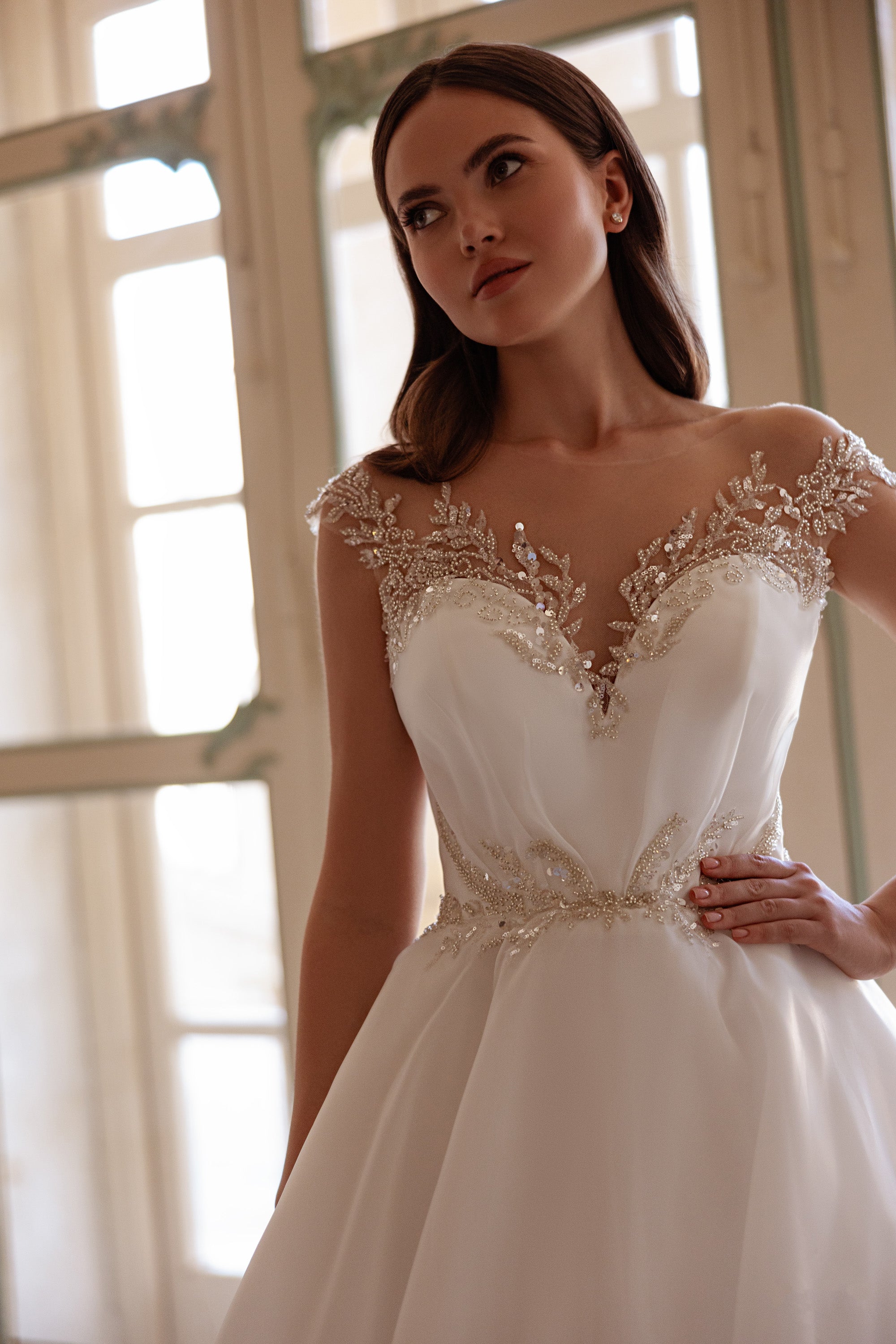 Close-up of an ivory wedding dress with a sheer beaded neckline and sparkling waist embellishment