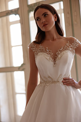 Close-up of an ivory wedding dress with a sheer beaded neckline and sparkling waist embellishment