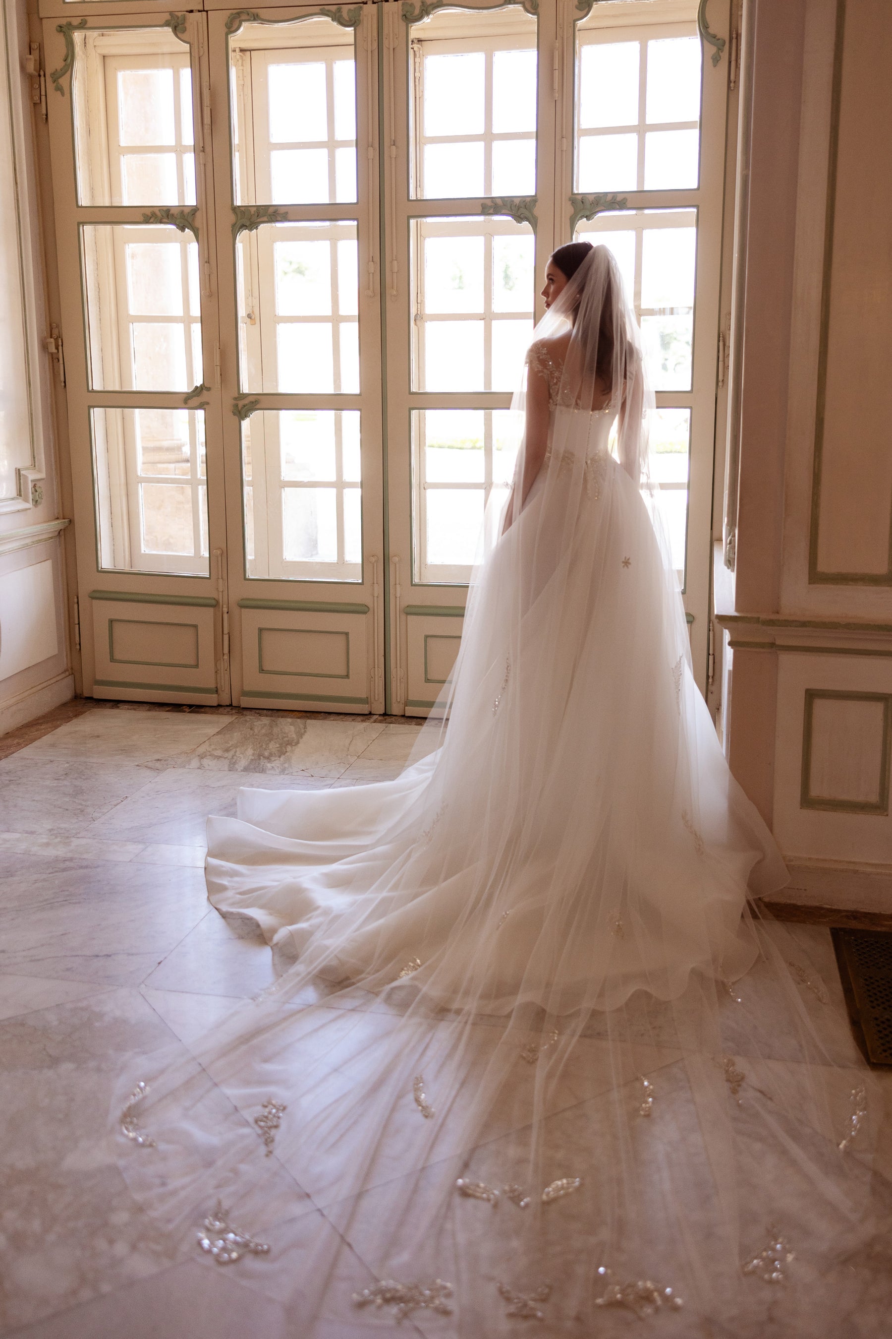 Wedding dress with a sheer embellished back and long, flowing train extending across the floor
