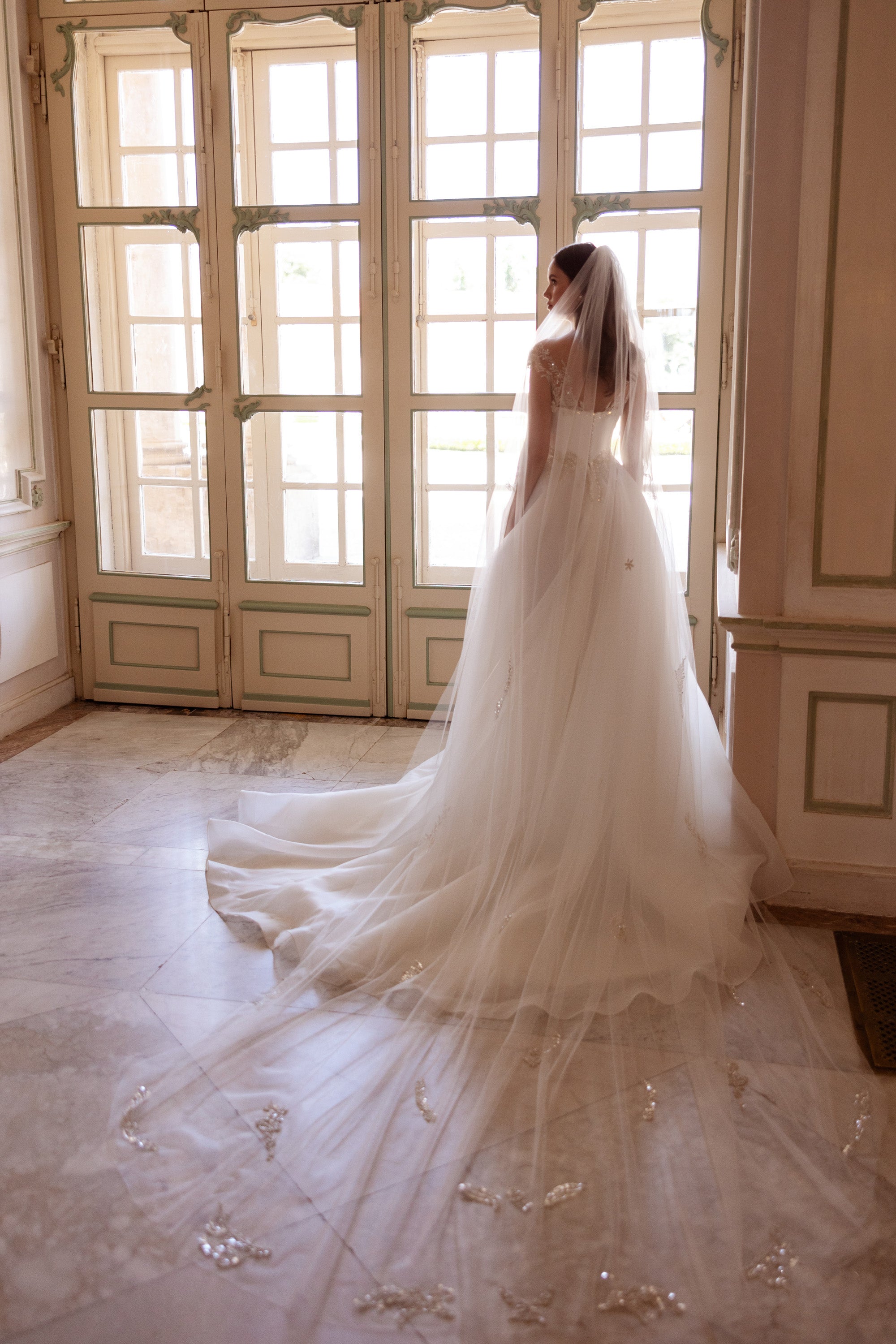 Wedding dress with a sheer embellished back and long, flowing train extending across the floor