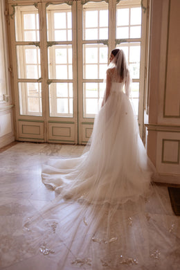 Wedding dress with a sheer embellished back and long, flowing train extending across the floor