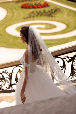 Side view of an ivory wedding dress with an off-shoulder pearl-beaded bodice and long flowing skirt