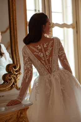 Ivory wedding dress with a deep illusion lace back, floral long sleeves, covered buttons, and a full A-line skirt