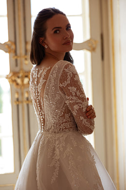 Close-up of an ivory wedding dress back with floral lace, sheer detailing, and a vertical row of covered buttons