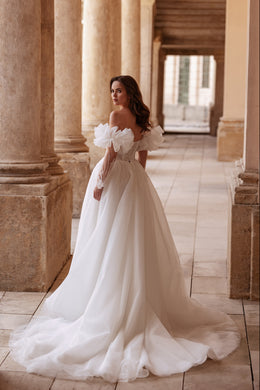 Ivory wedding dress with dramatic puff sleeves, a flowing A-line skirt, and a long gathered train seen from behind