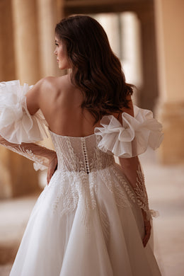 Open-back ivory wedding dress with a beaded corset bodice, puff sleeves, and a flowing train