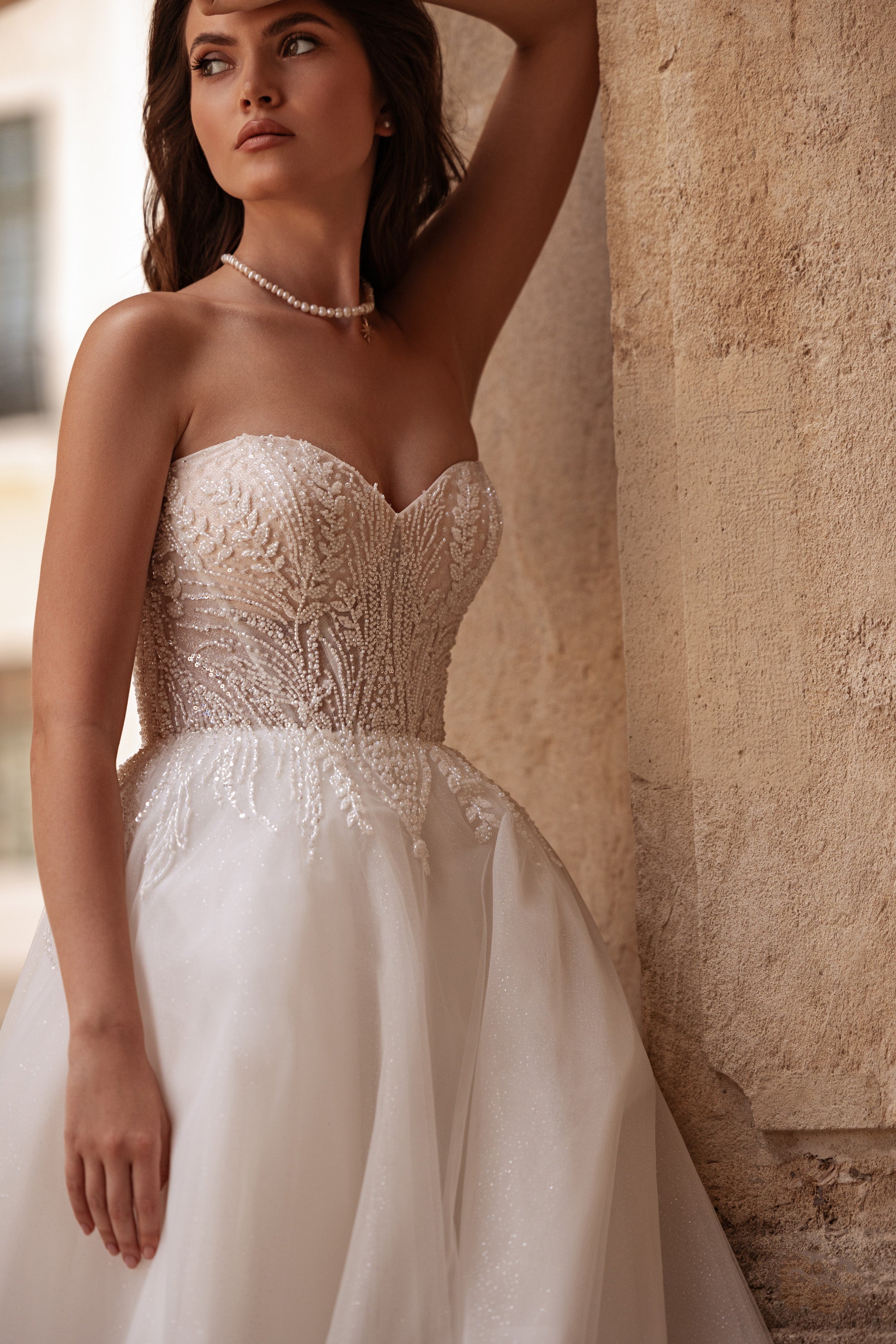 Close-up of an ivory wedding dress showing its beaded sweetheart neckline, fitted corset bodice, and shimmering skirt