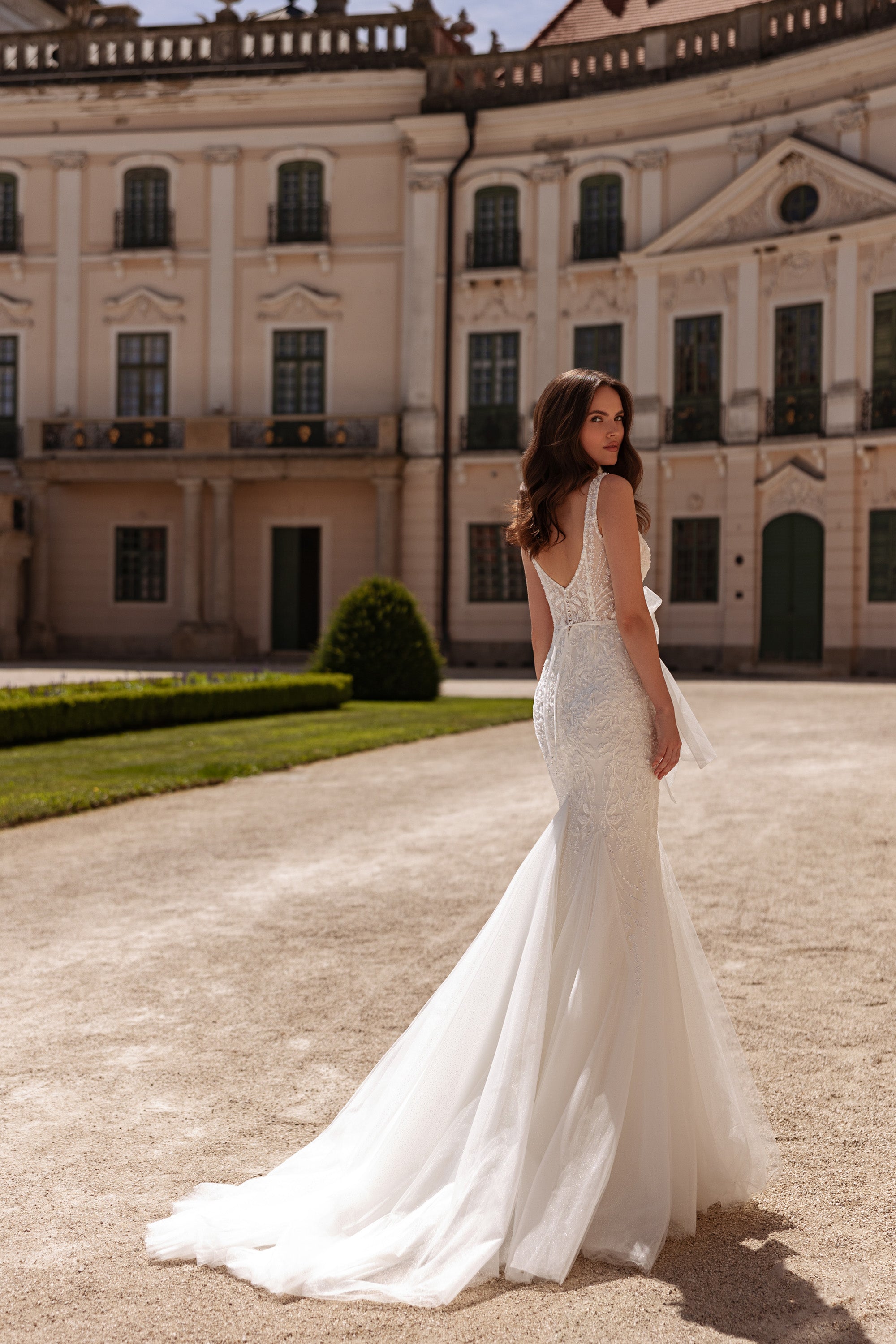 Back three-quarter view of an ivory mermaid wedding dress with a fitted shape and extended tulle train