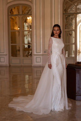 Ivory sheath wedding dress with a bateau neckline, long sheer beaded sleeves, and a flowing overskirt train