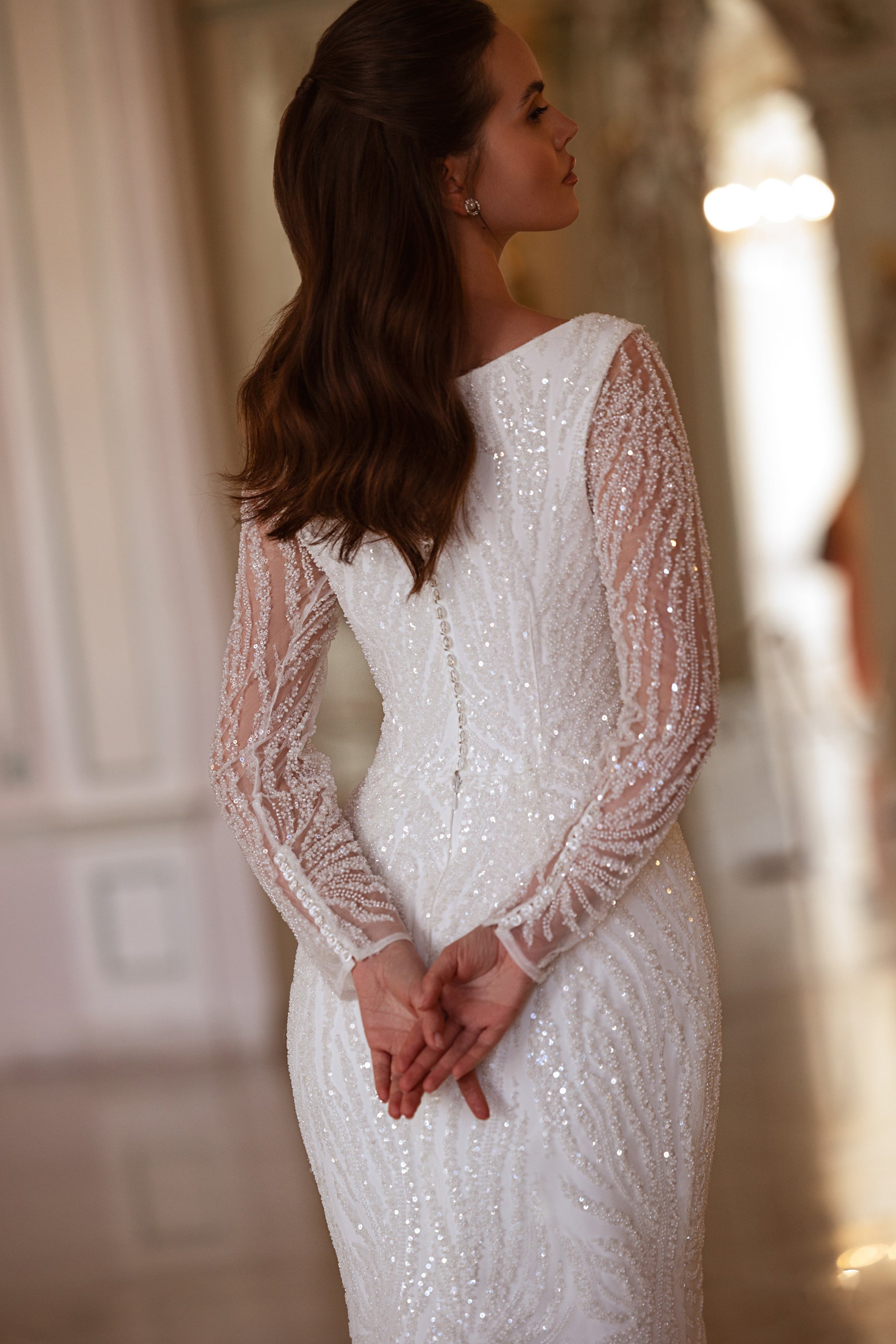 Closed-back ivory wedding dress with shimmering long sleeves and intricate beadwork across the fitted bodice