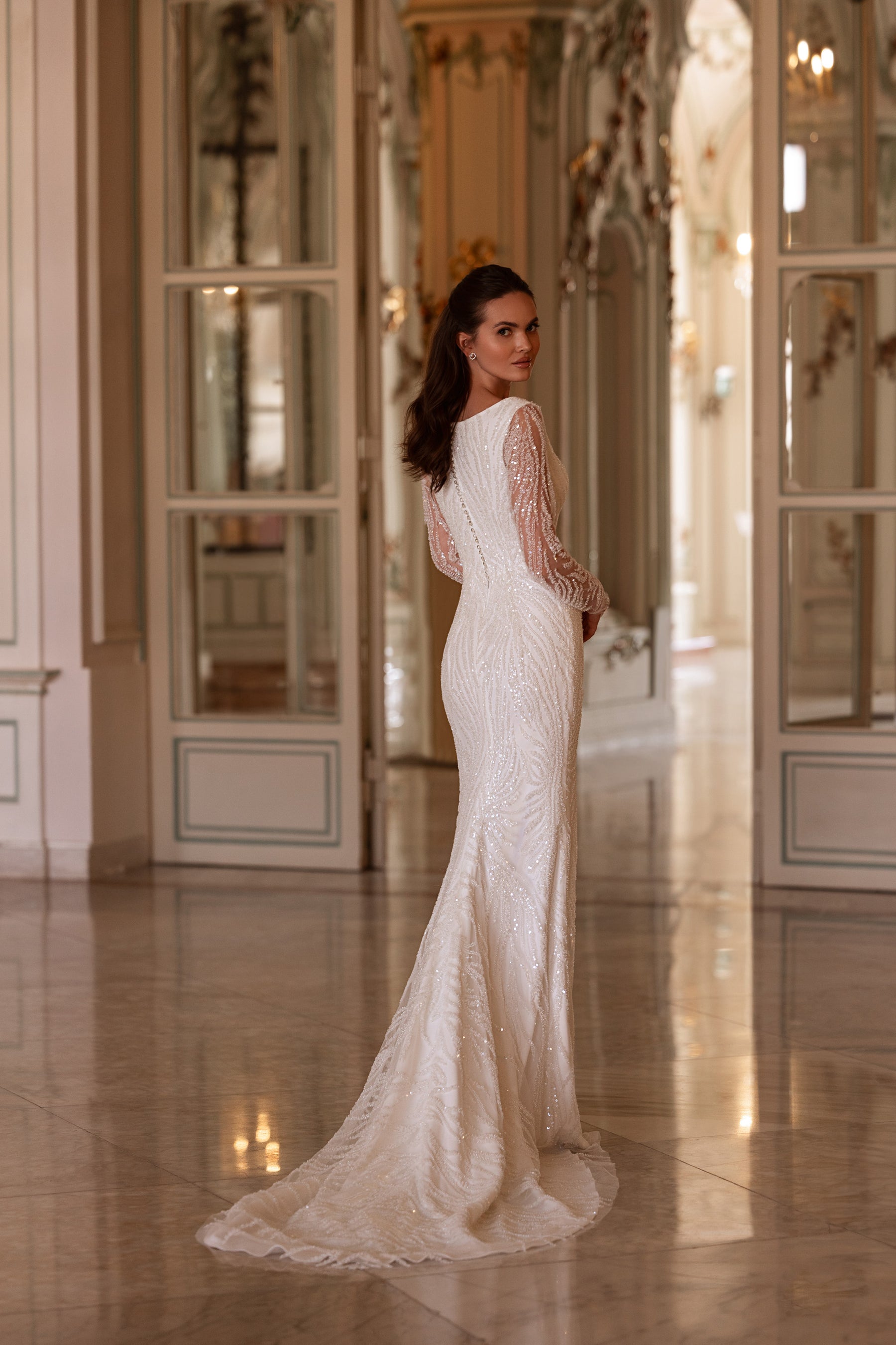 Three-quarter back view of an ivory sheath wedding dress with beaded sleeves and a sweeping floor-length train