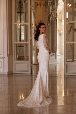 Three-quarter back view of an ivory sheath wedding dress with beaded sleeves and a sweeping floor-length train