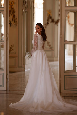 Back view of an ivory wedding dress with a gathered overskirt, beaded sleeves, and a wide flowing train