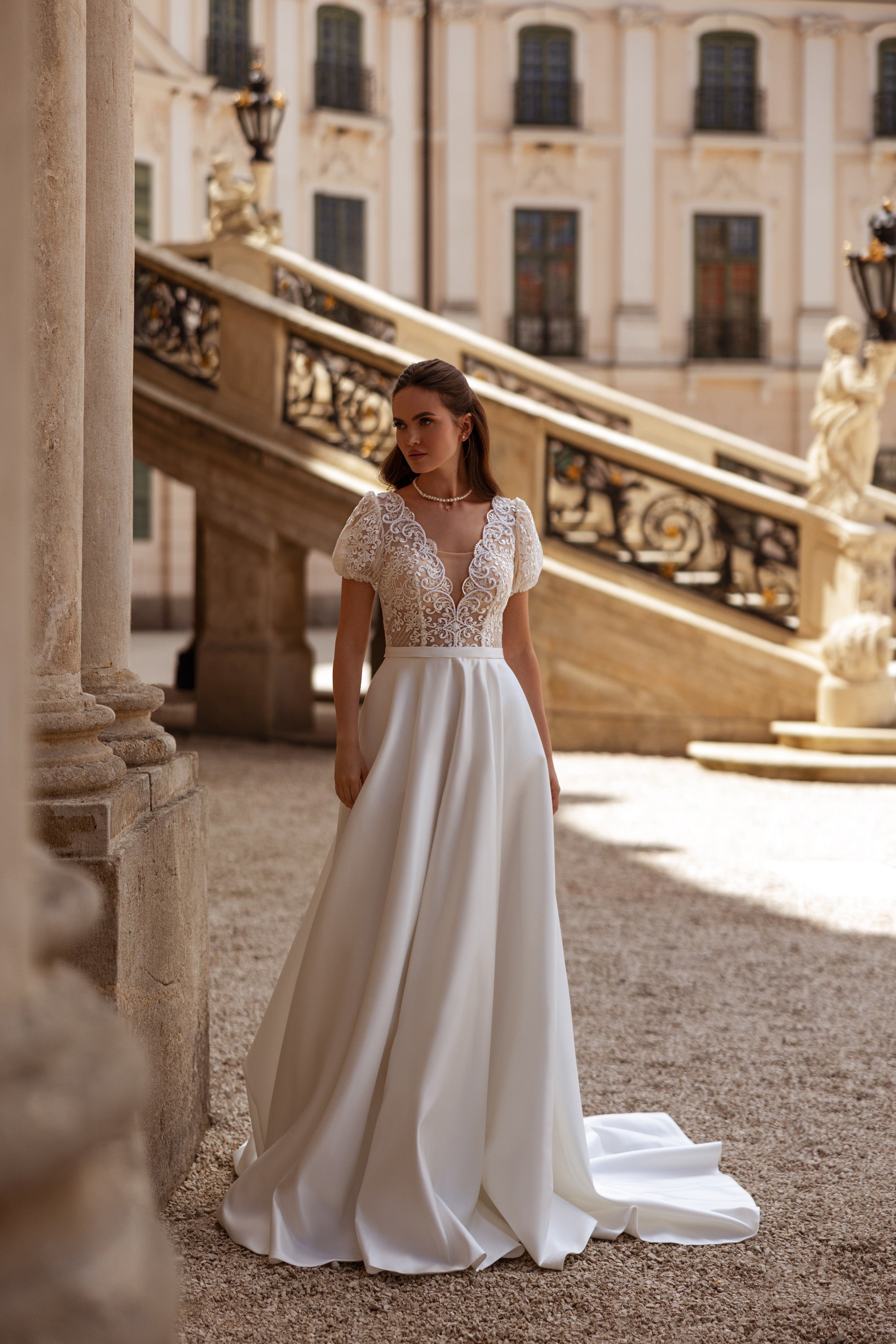 A-line ivory wedding dress with a deep V-neck lace bodice, puff sleeves, and sweeping train