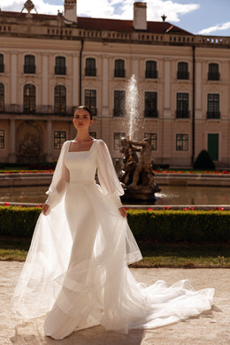 Ivory wedding dress with a square neckline, sheer bishop sleeves, fitted silhouette, and sweeping train