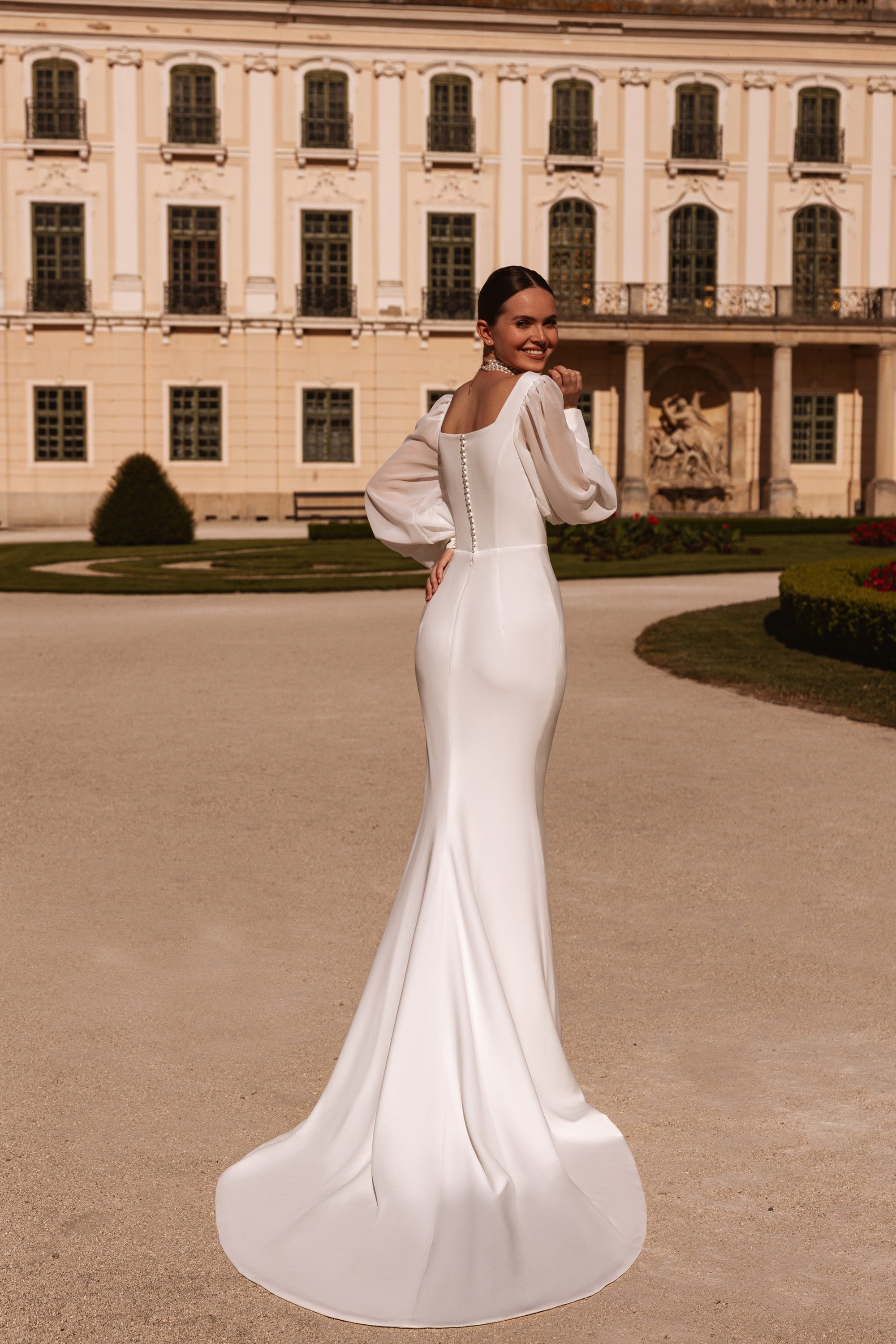 Back view of an ivory sheath wedding dress with bishop sleeves, fitted back, and smooth train