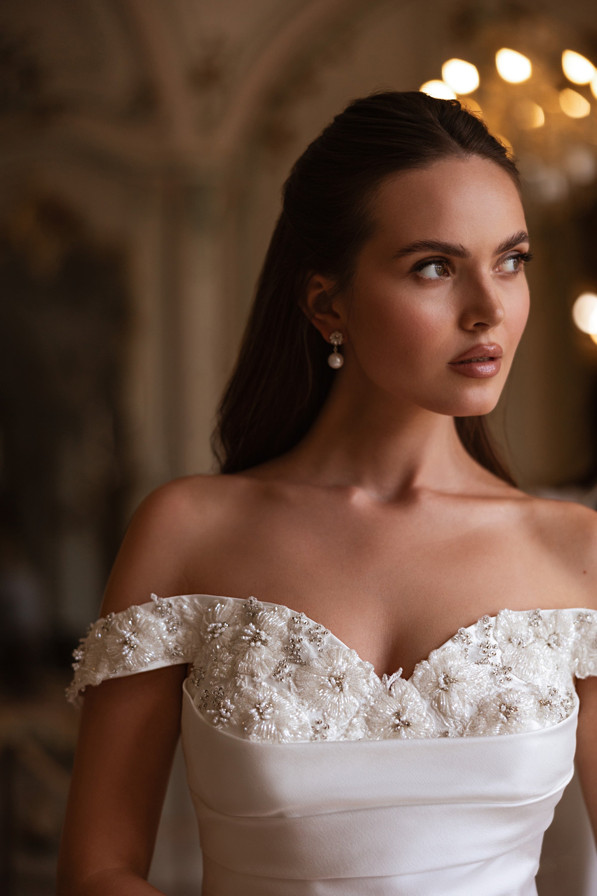 Close-up of an off-the-shoulder wedding dress bodice with floral lace, beadwork, and a sweetheart neckline