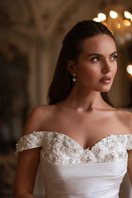 Close-up of an off-the-shoulder wedding dress bodice with floral lace, beadwork, and a sweetheart neckline