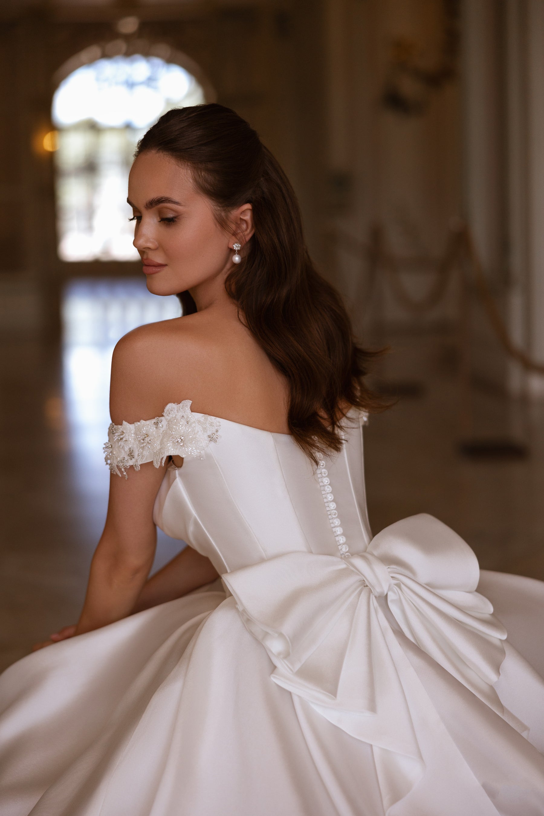 Back of an ivory wedding dress showing a large bow, covered buttons, and floral lace shoulder detail