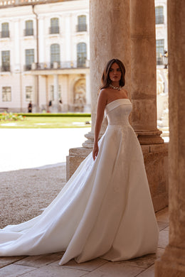 Ivory A-line wedding dress with a strapless bodice, floral lace details, and a long flowing train