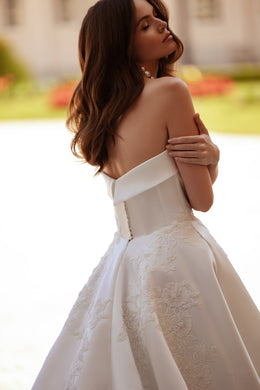 Bare-back ivory wedding dress with a folded strapless neckline, waist fastening, and floral lace skirt panels