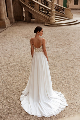 Wedding dress with an open lace-trimmed back, thin straps, flowing skirt, and long train