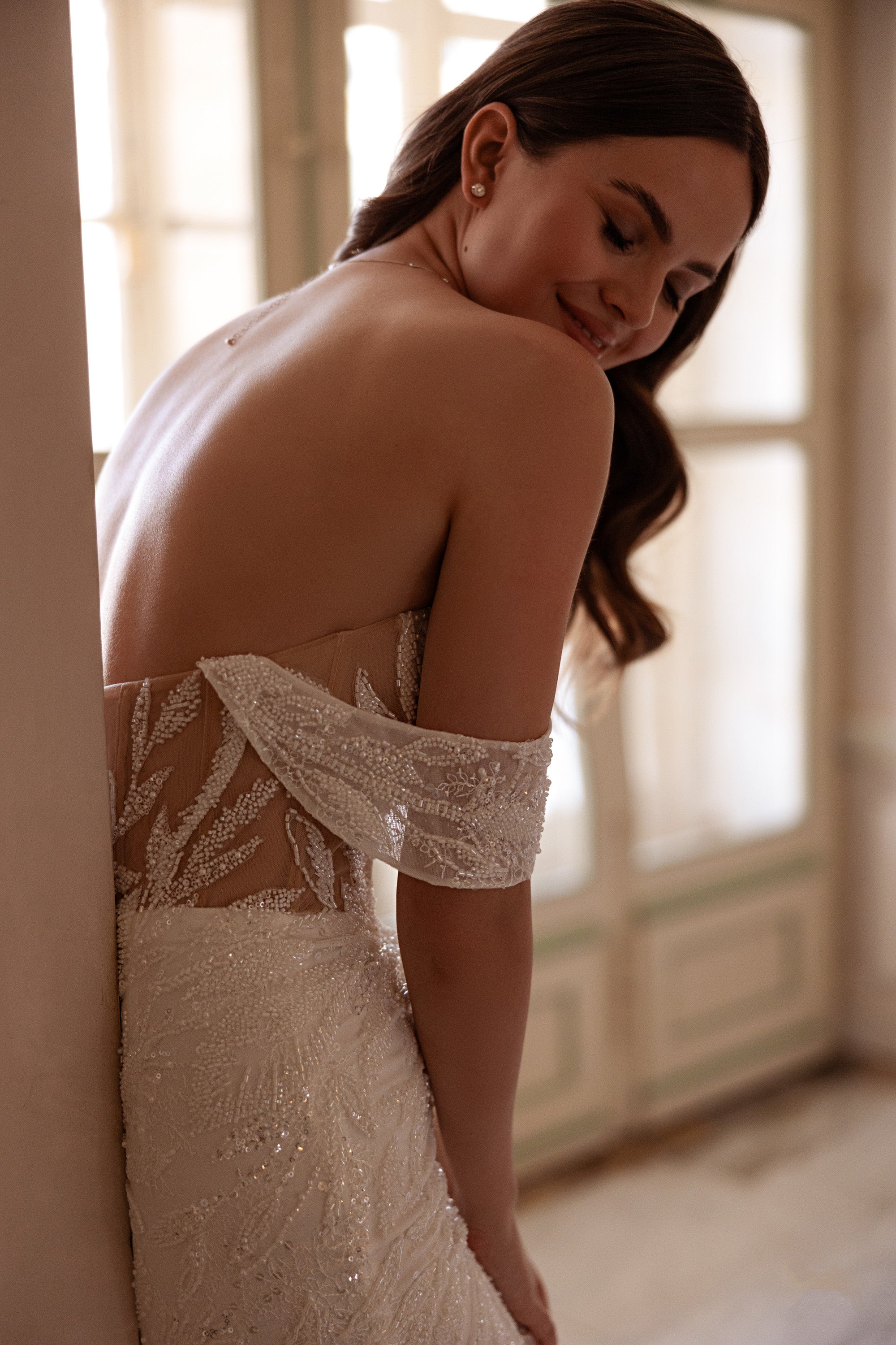 Open-back ivory wedding dress with beaded lace, off-the-shoulder sleeves, and a fitted mermaid silhouette