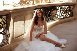 Seated white wedding dress showing a sheer corset bodice, lace appliqués, tulle skirt, and high front slit