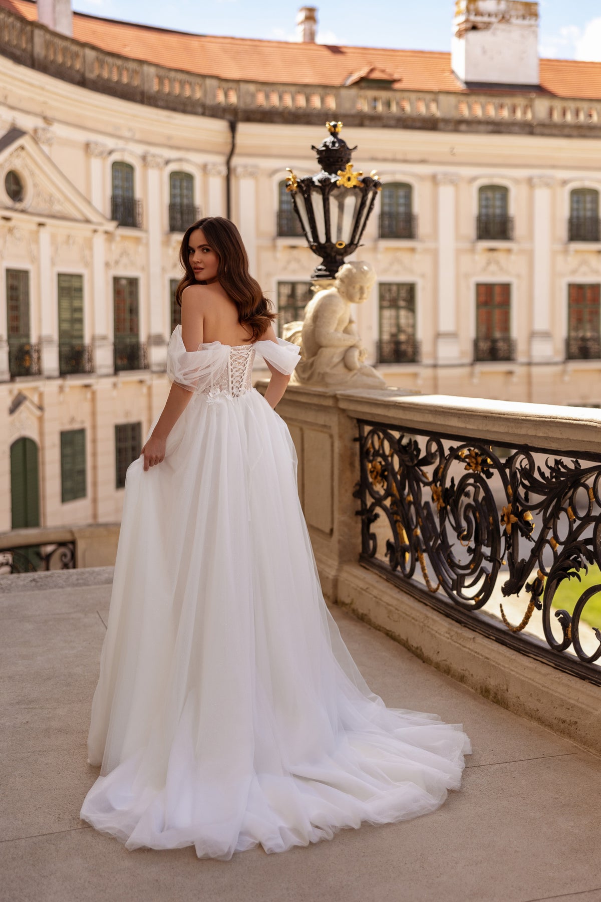 Back view of a white wedding dress with off-the-shoulder tulle sleeves, corset-style back, full skirt, and train