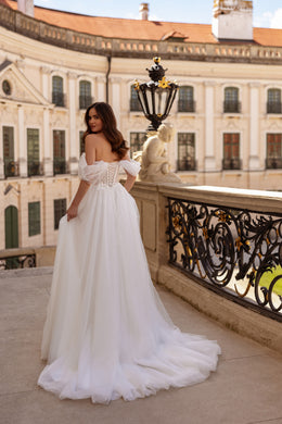 Back view of a white wedding dress with off-the-shoulder tulle sleeves, corset-style back, full skirt, and train