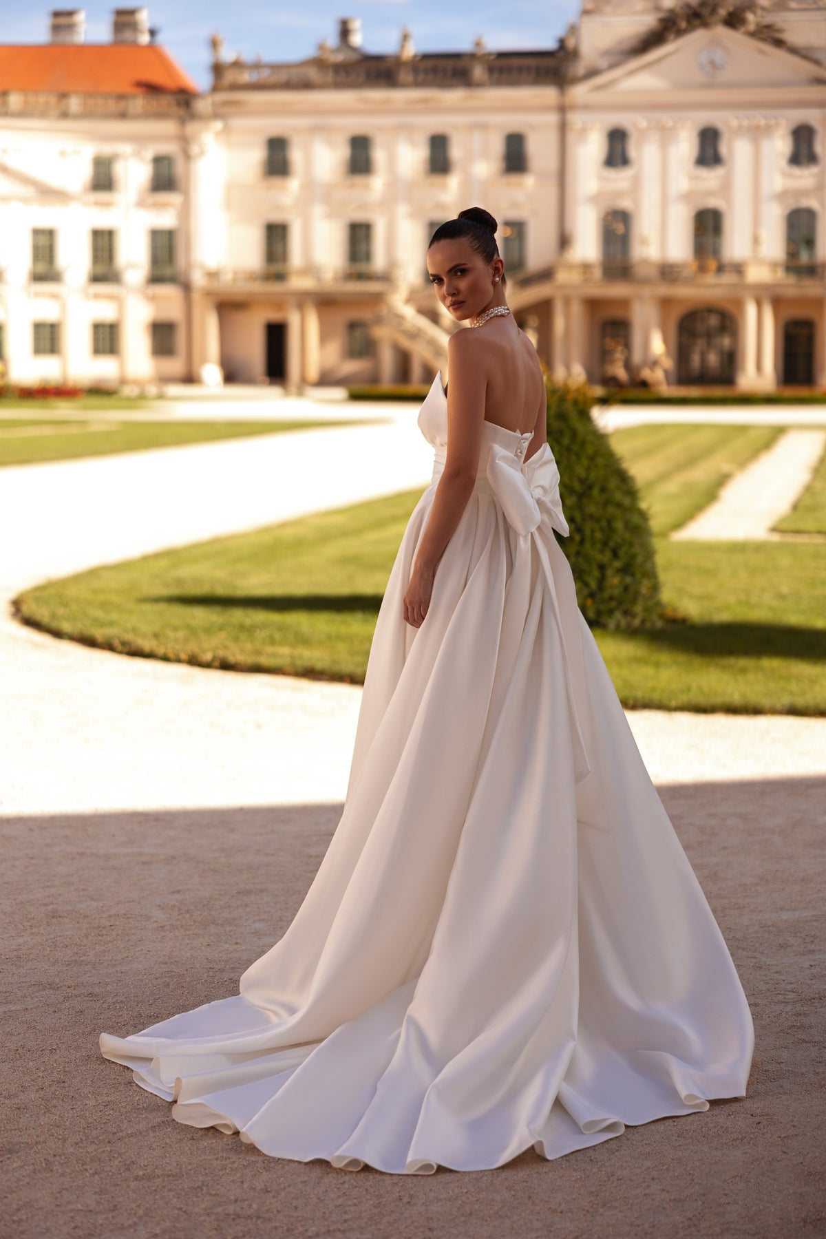 White wedding dress showing a low open back, draped sleeves, gathered waist, and sweeping floor-length train