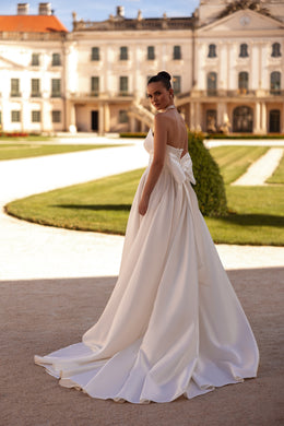 White wedding dress showing a low open back, draped sleeves, gathered waist, and sweeping floor-length train