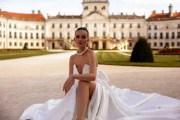 White wedding dress with a deep V neckline, voluminous draped skirt, high slit, and long train spread on the ground