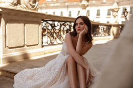 Glittering A-line wedding dress with beaded straps and a flowing skirt draped beside the seated wearer