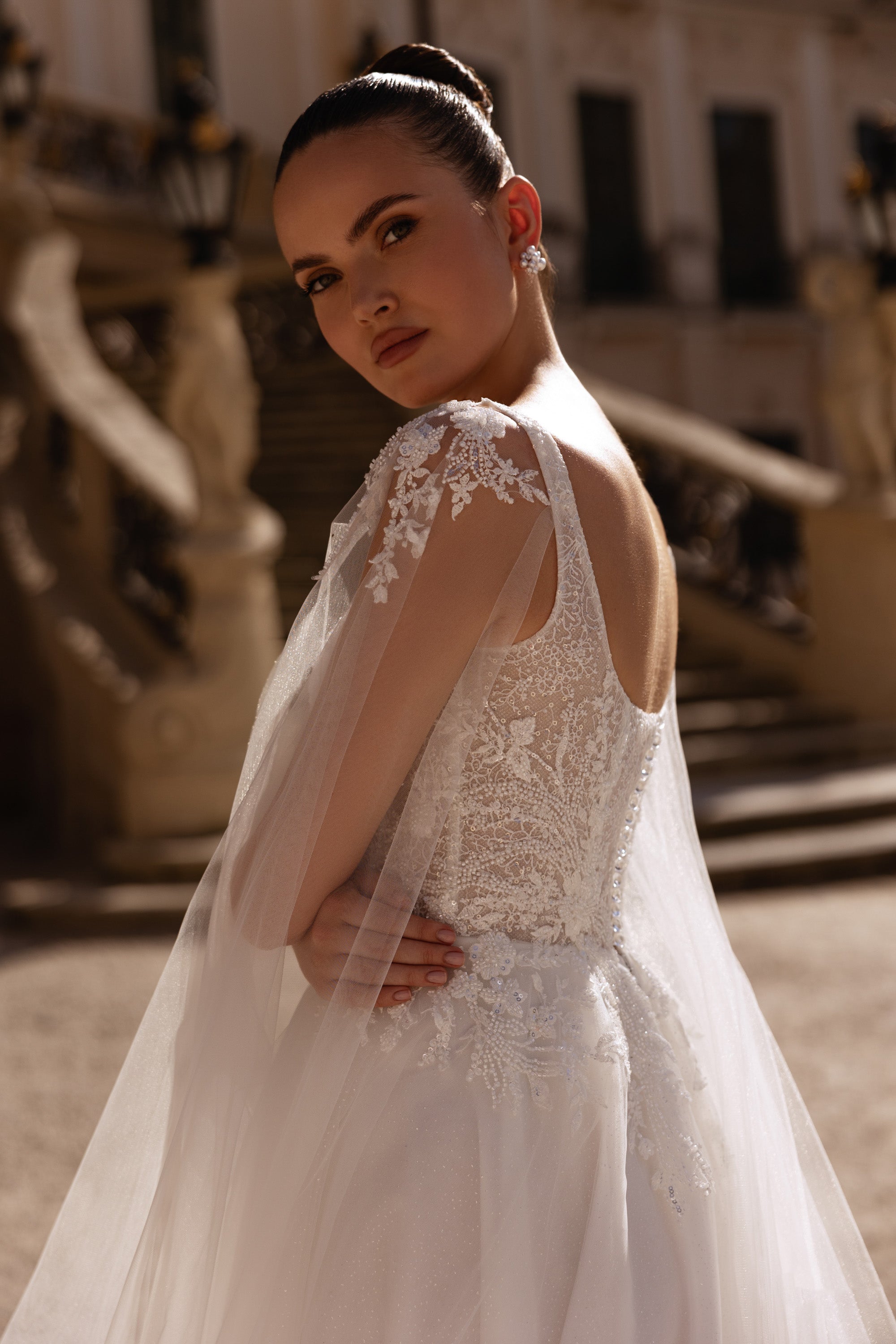 Ivory wedding dress with an open lace back, floral lace bodice, and sheer detachable cape