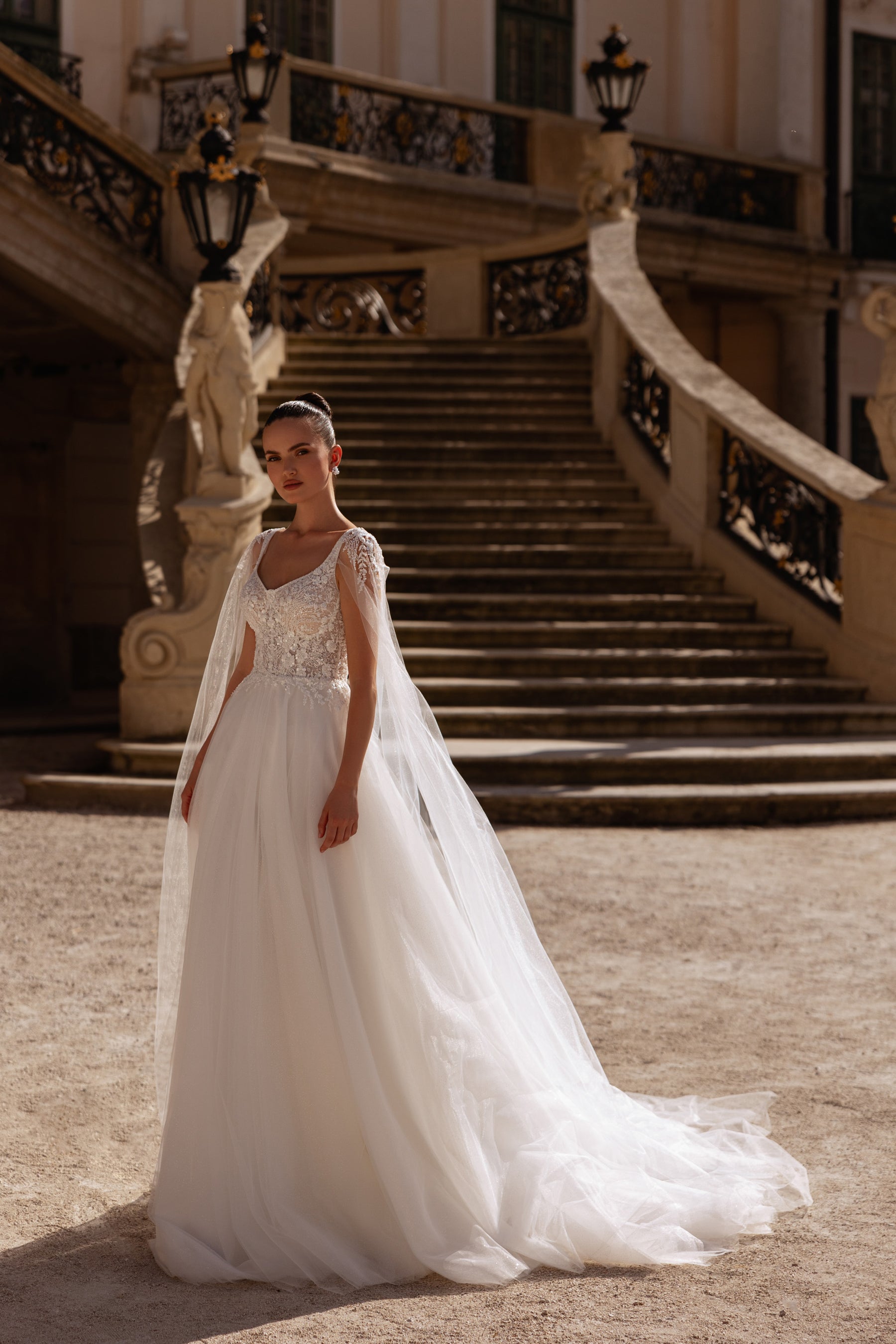 Ivory A-line wedding dress with a sleeveless floral lace bodice, scoop neckline, and long sheer cape