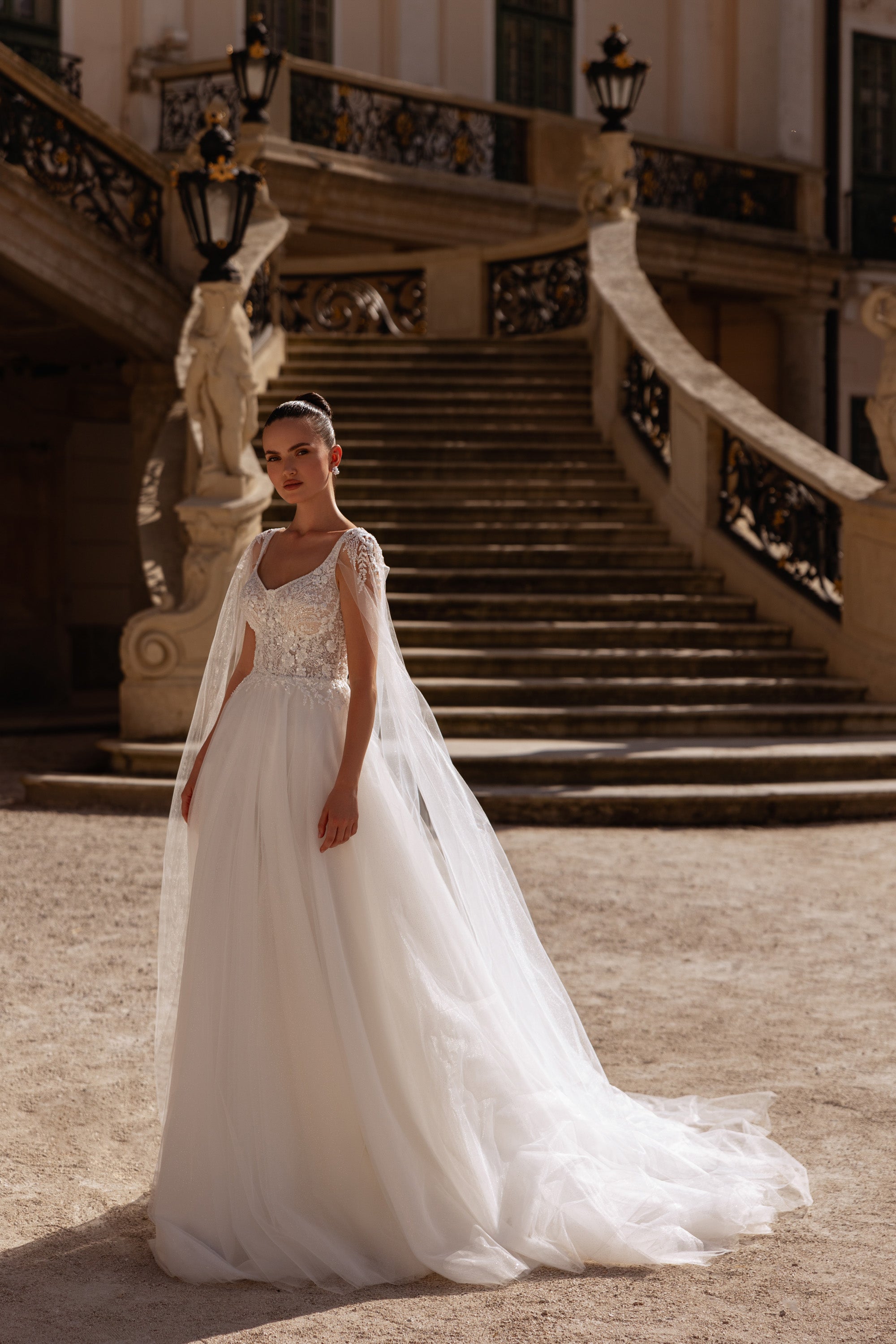 Ivory A-line wedding dress with a sleeveless floral lace bodice, scoop neckline, and long sheer cape