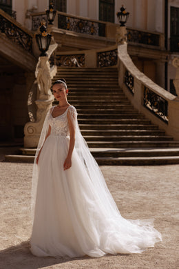 Ivory A-line wedding dress with a sleeveless floral lace bodice, scoop neckline, and long sheer cape