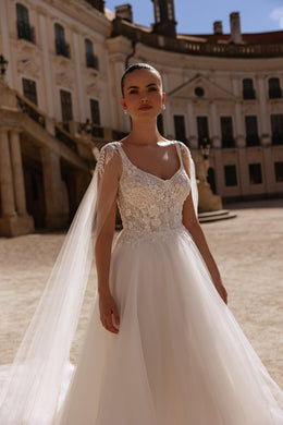 Ivory wedding dress featuring a beaded floral lace bodice, scoop neckline, and flowing detachable cape