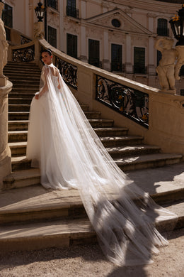 Back view of an ivory wedding dress with a sheer cape cascading into a long train